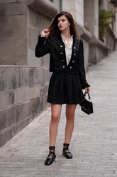 a lady in a white ruffle collared shirt, a black tweed jacket and a black tweed mini skirt